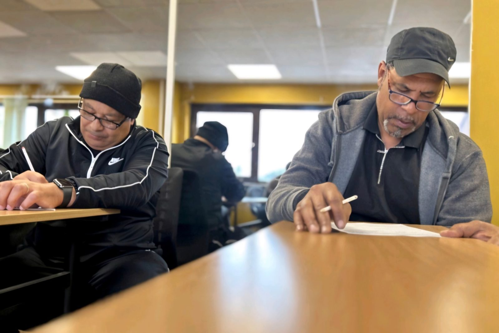 Two learners in the training room working through their papers on a refresher day.