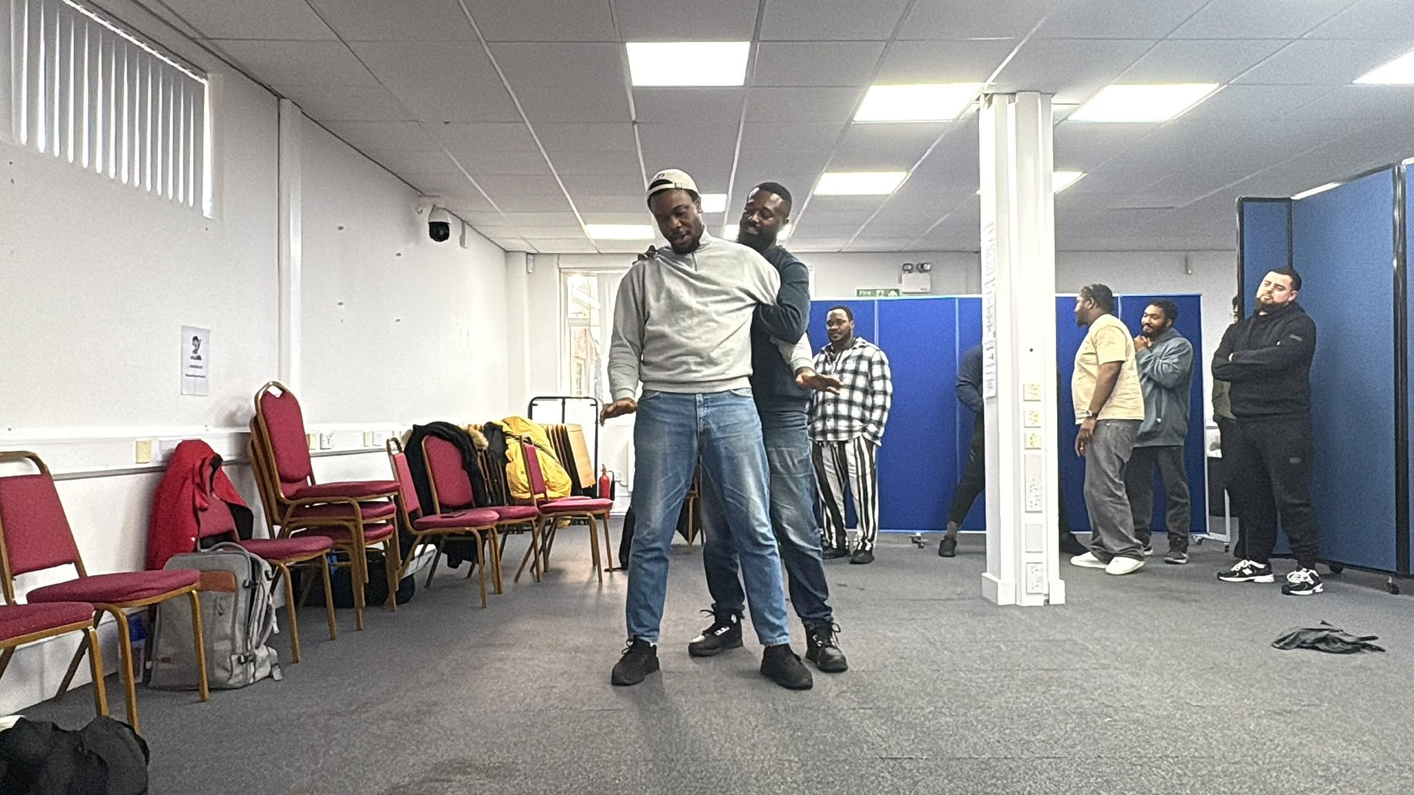 Two learners practising a controlled hold in the training room while others watch.