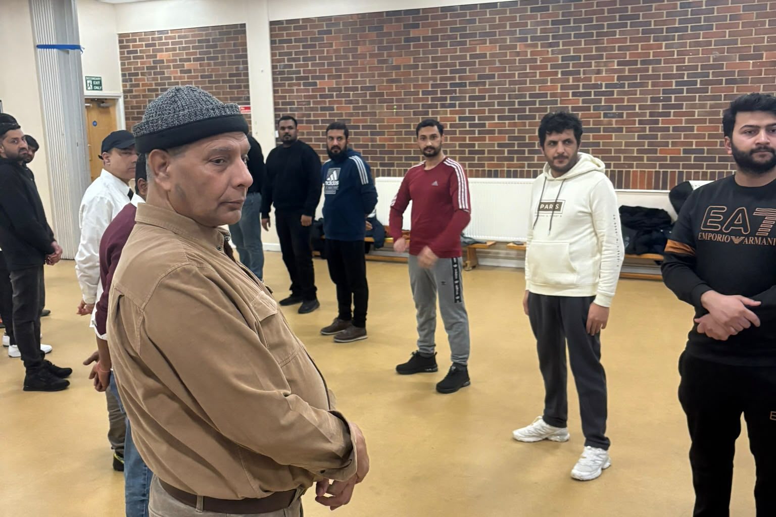 A trainer addressing a class standing in a circle in a community hall.